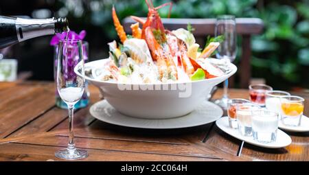 Cameriere che versa vino bianco in un bicchiere di vino e serve al cliente al ristorante con grande ciotola di pesce su ghiaccio in background. Ristorante gastronomia cibo Foto Stock