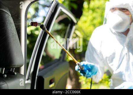 Primo piano di pulizia a spruzzo con alcool chimico all'interno dell'auto per disinfettare e decontaminare il coronavirus covid-19 da un detergente specializzato che indossa il prodotto personale Foto Stock