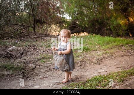 Un bambino raccoglie i rifiuti nella foresta, una bambina porta una bottiglia di plastica contro uno sfondo di splendidi alberi. Il bambino ha trovato una spazzatura può Foto Stock