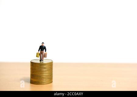 Un uomo che si trova sopra la pila di monete per proteggere i soldi. Fotografia concettuale di figure di persone in miniatura. Foto Stock