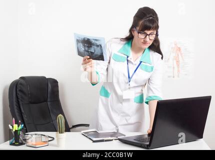 Il radiologo medico tiene un'immagine radiografica della mascella dentaria e controlla i dati in un computer portatile, in un ufficio medico in clinica. Diagnostica radiazioni con Foto Stock