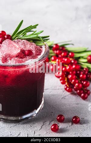 Cocktail di frutta fresca ghiacciata in vetro, rinfrescante bevanda estiva al ribes rosso con foglia di rosmarino su fondo di pietra in cemento, vista angolare Foto Stock