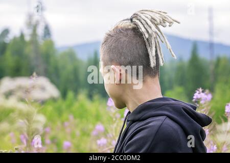 Ritratto di un giovane ragazzo con dreadlock sullo sfondo di un parco forestale e montagne. Vista dal retro. Spazio di copia Foto Stock