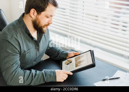 Tecnico che lavora con grafici e diagrammi su tablet in ufficio. Foto Stock