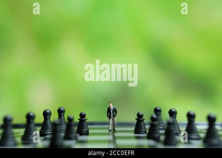 Strategia di business foto concettuale - miniatura di uomo d'affari che cammina in avanti nel mezzo del pezzo di scacchi su una scacchiera Foto Stock