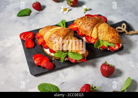 Colazione gustosa. Croissant freschi con fragole su fondo di cemento Foto Stock