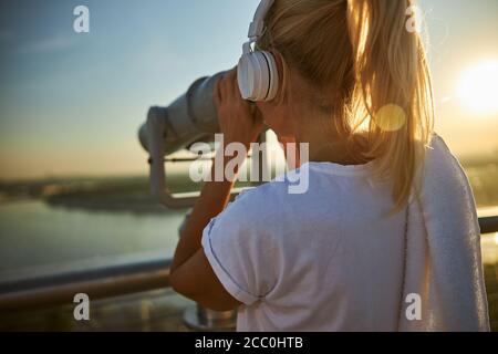 Donna in cuffia con binocolo di osservazione per strada Foto Stock