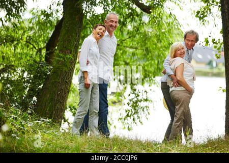 Due coppie di anziani ridenti prendono una passeggiata intorno a. lago d'estate Foto Stock