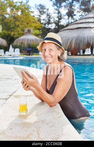 Smiling Senior Woman in Pool con Tablet computer legge un EBook in vacanza Foto Stock