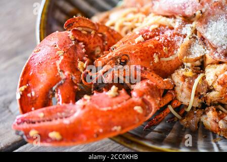 Piatto di frutti di mare di molluschi con cena di aragosta cucinata / grigliata Aragosta salsiccia prosciutto verdure e formaggio spaghetti frutti di mare su legno tabella Foto Stock