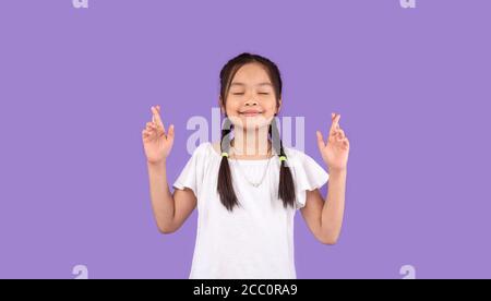 Asian Little Girl che tiene le dita incrociate facendo desiderio in Studio Foto Stock