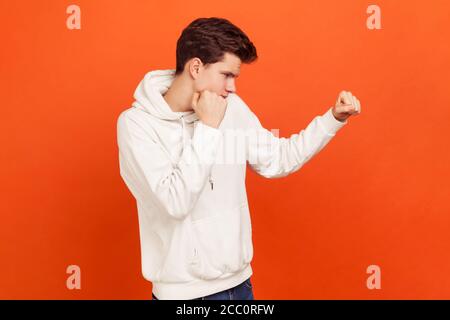 Combattente maschile in felpa con cappuccio che tiene pugni aggrappati, pronti ad attaccare. Giovane uomo che difende dai bulli. Lezioni di scuola d'arte marziale. Studio interno girato è Foto Stock