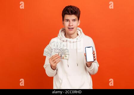 Uomo estremamente sorpreso in hodie casual che tiene molto dollari e smartphone con display vuoto per la pubblicità, scioccato con cashback, Internet divieto Foto Stock