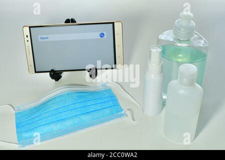 Foto ad alto angolo di un cellulare, bottiglie di disinfettante e una maschera facciale su una superficie bianca Foto Stock