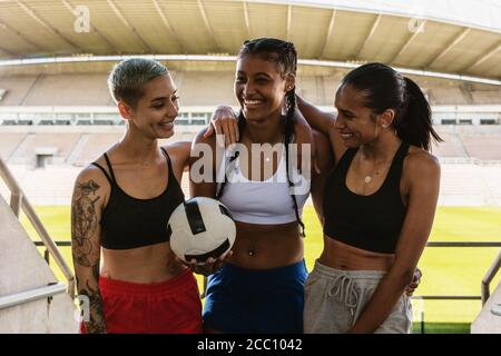 Gruppo di tre calciatori femminili allo stadio. Una squadra di calcio femminile con una palla che esce dallo stadio dopo una sessione di allenamento. Foto Stock