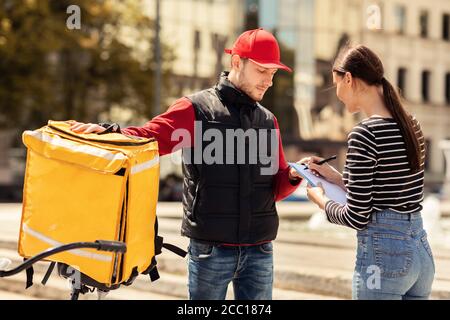 Customer Girl Signing Papers in piedi con Delivery Guy Outdoors Foto Stock