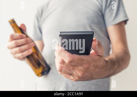 Bere birra e utilizzare lo smartphone, primo piano delle mani maschili con messa a fuoco selettiva Foto Stock