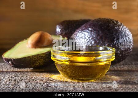 Vaso con olio e avocado fresco maturo su un rustico tavolo in legno vecchio. Il concetto di alimentazione sana e nutrizione. Composizione in stile vintage. Foto Stock