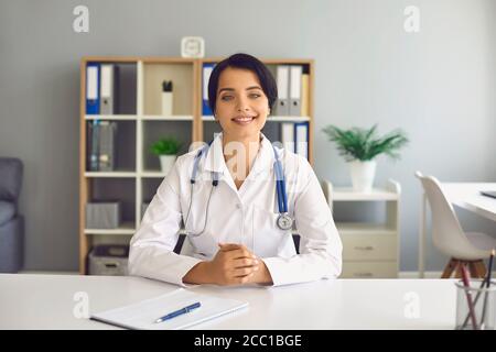 Una dottoressa in un camice bianco guarda nella telecamera di un computer portatile e consulta un paziente utilizzando un'applicazione di videochiamata clinica. Foto Stock