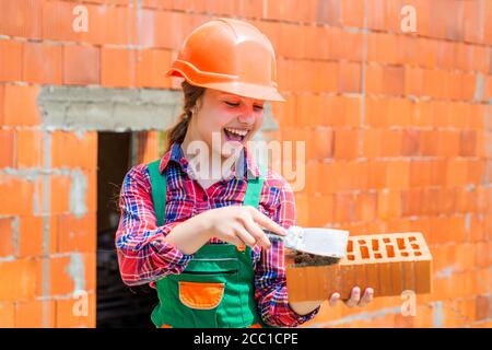 lay bricks. ingegnere teen è lavoratore di costruzione. Artigiano o operaio professionista. International workers day. Ragazza in casco gioca costruttore con mattone. Costruire una casa. Costruzione di capretti. Foto Stock