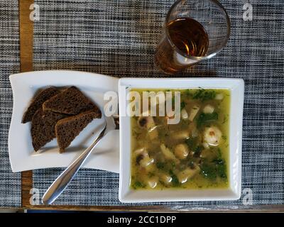Zuppa di funghi con pancetta. Servito su un vassoio di porcellana riccia in un recipiente profondo con cracker. Nelle vicinanze si trova un bicchiere di succo Foto Stock