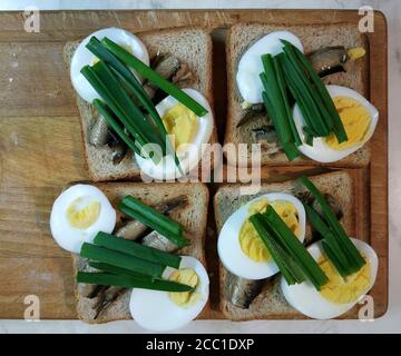 Panini con spratti e uova, decorati con cipolle verdi. Servito su un asse di legno per tagliare le verdure Foto Stock