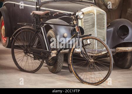 Antica bicicletta arrugginita e auto nera in un vecchio capannone Foto Stock
