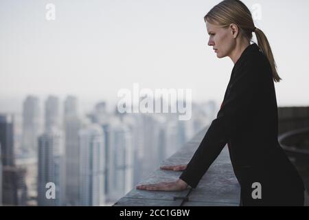 Preoccupata giovane uomo d'affari che pensa mentre si guarda alla vista della città da un tetto di grattacieli. Business, carriera e stress lavorativo. Foto Stock