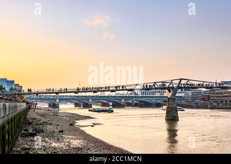 Pendolari e turisti che attraversano il Millennium Bridge in una serata autunnale, retroilluminata dal tramonto, Bankside, Londra, Regno Unito Foto Stock