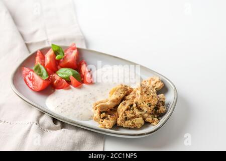 Pezzi di pollo marinato orientale, salsa al sesamo allo yogurt e pomodori con guarnitura al basilico, serviti su un piccolo piatto su un tavolo bianco, spazio copia, sele Foto Stock