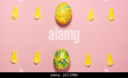 Coniglietti gialli di velluto e uova di pasqua su sfondo rosa in alto e in basso con spazio per il testo. Vista dall'alto in posizione piatta. Concetto di Pasqua Foto Stock