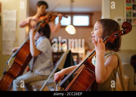 Un bambino felice gioca il violoncello con la famiglia in sottofondo musica Foto Stock