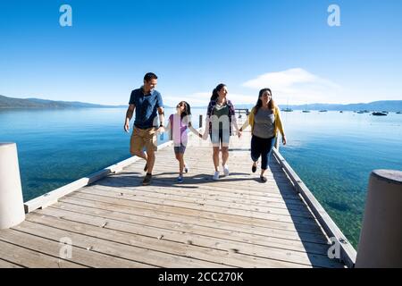 Una famiglia sorride e tiene le mani a piedi giù un molo in una giornata di sole a South Lake Tahoe, California. Foto Stock
