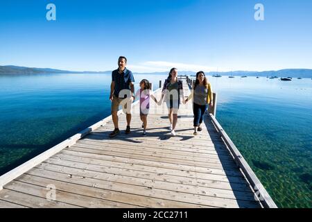 Una famiglia sorride e tiene le mani a piedi giù un molo in una giornata di sole a South Lake Tahoe, California. Foto Stock