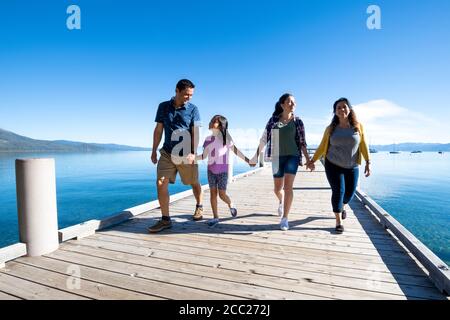 Una famiglia sorride e tiene le mani a piedi giù un molo in una giornata di sole a South Lake Tahoe, California. Foto Stock