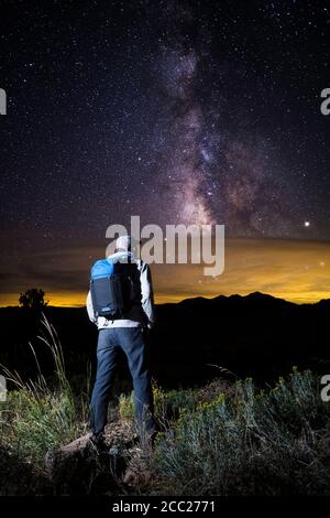 Un uomo che indossa uno zaino si trova illuminato vicino alla Sierra Nevada Mountain Range mentre si guarda lo splendido cielo notturno da Monitor Pass, Califo Foto Stock