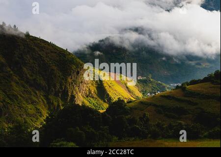 L'alta Himalaya sotto il tappeto di nuvole avvolse un piccolo villaggio rurale in lontananza alle pause all'alba in estate vicino a Tawang, Arunachal Pradesh, India. Foto Stock