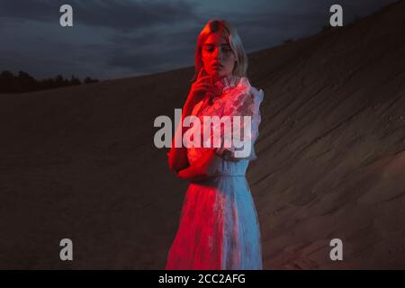 Donna in un lungo vestito in piedi vicino a una collina sabbiosa di sera Foto Stock
