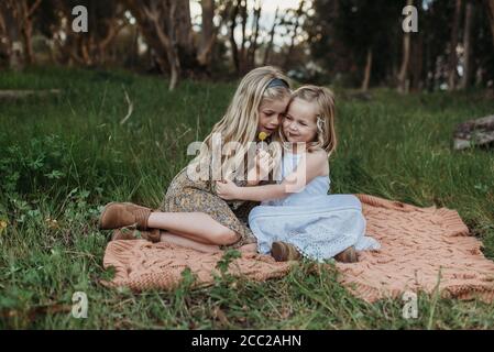 Due sorelle bionde sedute su una coperta in un campo con lollipop Foto Stock