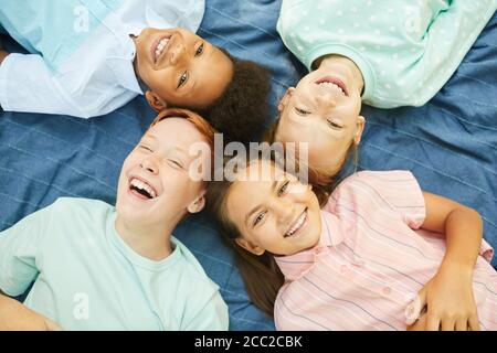 Vista dall'alto di un gruppo multietnico di bambini che mentono in cerchio su coperta all'aperto e guardando la fotocamera Foto Stock