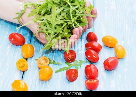 insalata di rucola in mani femminili accanto ai pomodori ciliegini rosso e giallo. Foto Stock