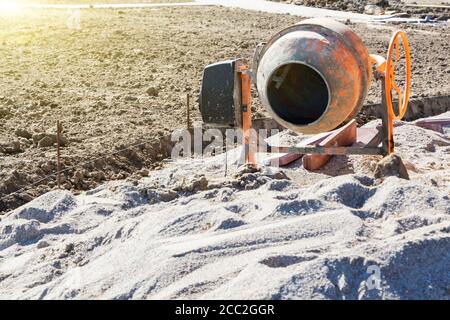 Betoniera mobile si trova accanto a una pila di ghiaia sul cantiere. Foto Stock