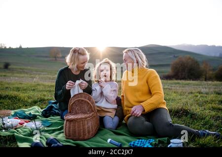 Bambina con madre e nonna che hanno pic-nic in natura al tramonto. Foto Stock