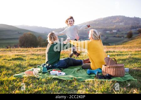 Bambina con madre e nonna che hanno pic-nic in natura al tramonto. Foto Stock