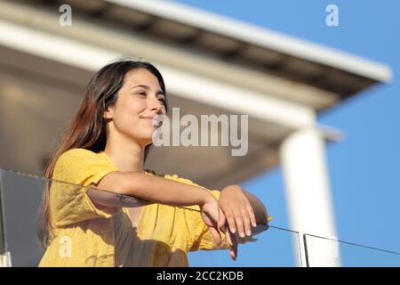 Donna soddisfatta in giallo contemplando le viste in un balcone sopra estate Foto Stock