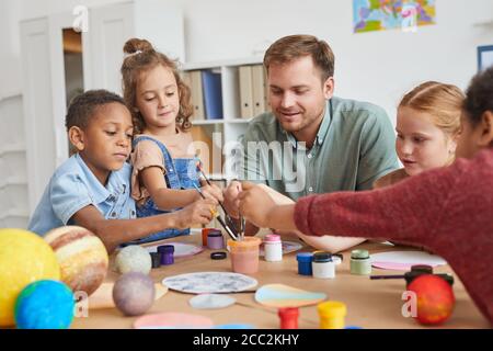 Ritratto di un gruppo multietnico di bambini che tengono pennelli e dipinti modello del pianeta mentre godendo l'arte e la lezione di artigianato a scuola o il cent. di sviluppo Foto Stock