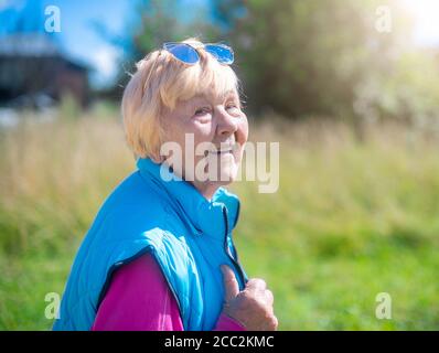 Nonna felice, alla moda di 90 anni con i capelli grigi e un sorriso nella natura in una giornata estiva di sole. Foto Stock