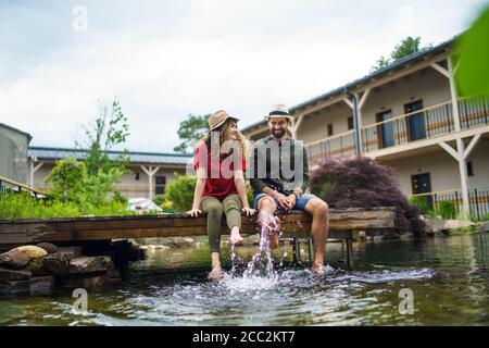 Giovane coppia che si siede all'aperto vicino all'hotel sul lago in vacanza, divertendosi. Foto Stock