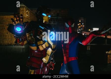 Due cosplayer si levano in piedi insieme nelle immagini di un personaggio Spider-Man e Iron Man contro il paesaggio urbano e le luci notturne. Foto Stock