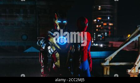 Due cosplayer si levano in piedi insieme nelle immagini di un personaggio Spider-Man e Iron Man contro il paesaggio urbano e le luci notturne. Foto Stock